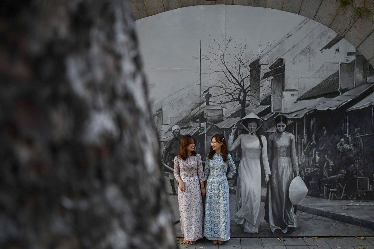 Vietnamese women pose for photographs in front of a mural on a street in Hanoi on 18 October 2019. Photo: AFP