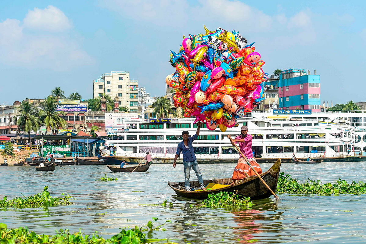 A man holds balloons as he crosses the Buriganga river on a boat in Dhaka on 18 October 2019. Photo: AFP