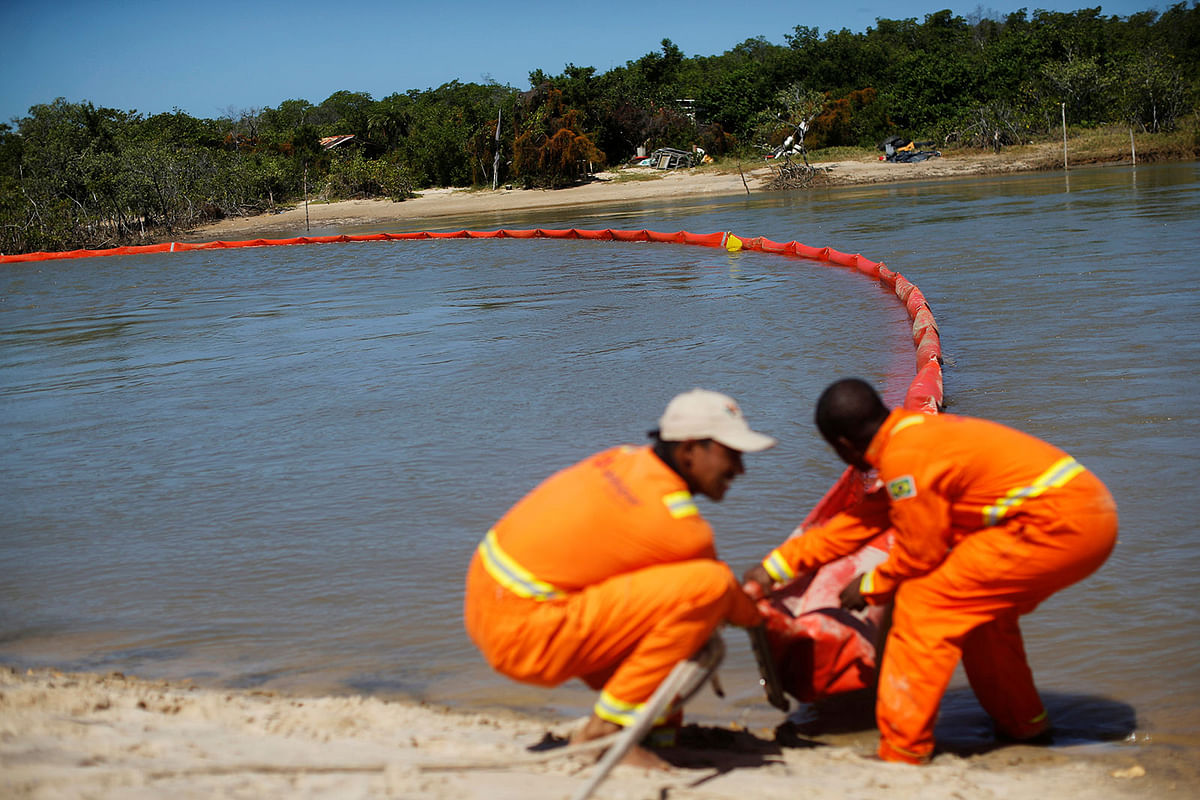 Men work on oil containment booms on the river next to Viral beach in Aracaju, Sergipe state, Brazil on 13 October 2019. Photo: Reuters