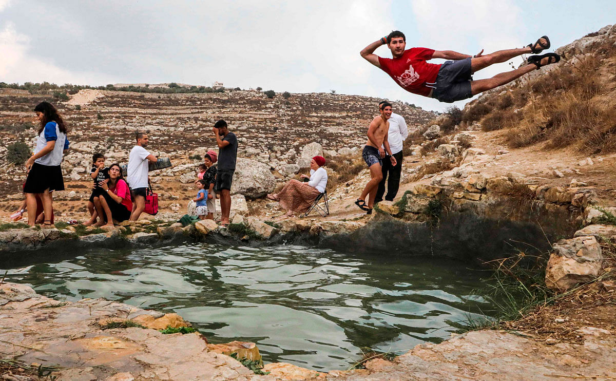 Israelis sit by as a man poses while jumping into the pool of the natural water spring of Ein al-Faraah near the Palestinian village of Doura, west of Hebron in the occupied West Bank, during the Jewish religious holiday of Sukkot (Feast of the Tabernacles) on 17 October 2019. Photo: AFP