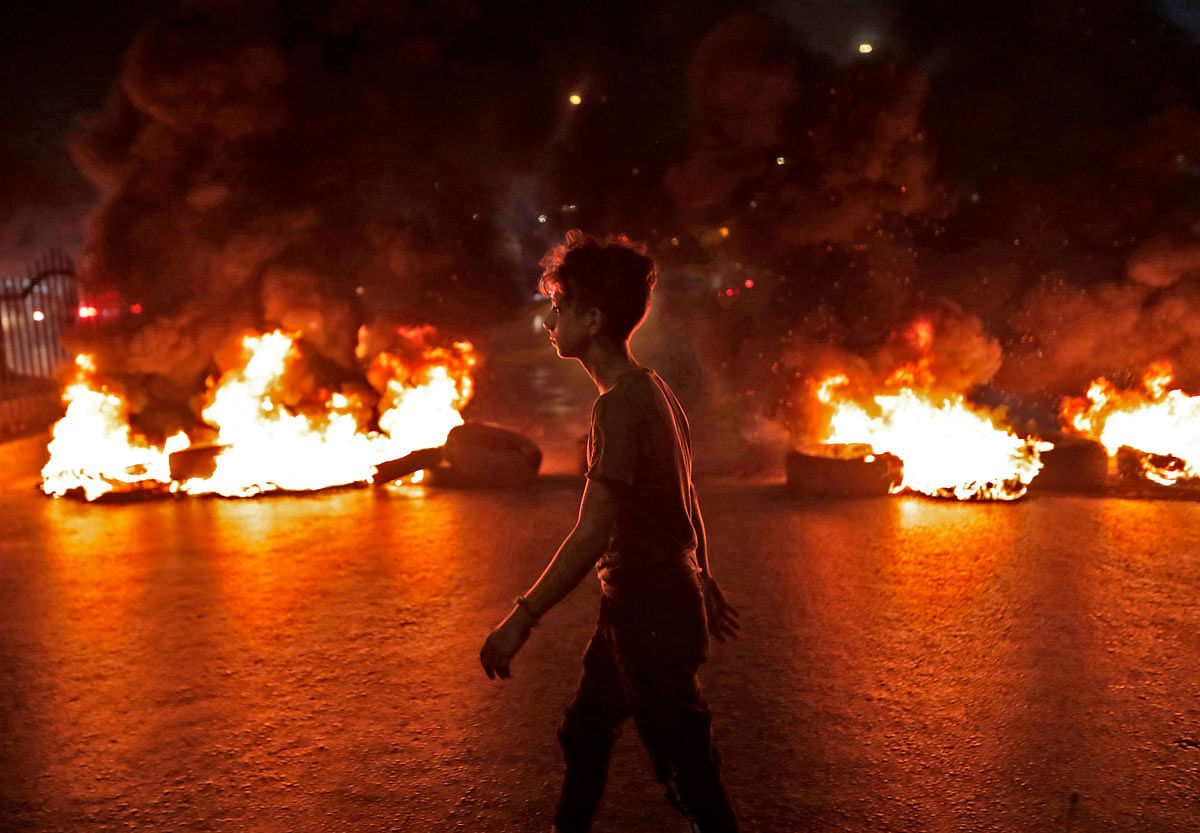 A Lebanese demonstrator walks past burning tires during a protest against recent tax calls on 17 October 2019 in the southern suburbs of Beirut. Hundreds took to the streets across Lebanon Thursday to protest dire economic conditions after a government decision to tax calls made on messaging applications sparked widespread outrage. Photo: AFP