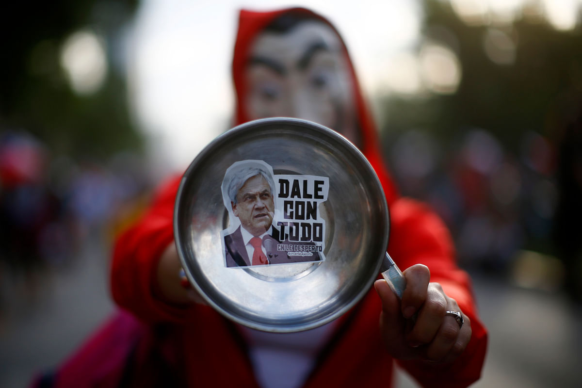 A masked demonstrator holds a pot depicting Chilean President sebastian Pinera reading `Hit him hard` in Santiago, on 25 October 2019, a week after violent protests started. Photo: AFP
