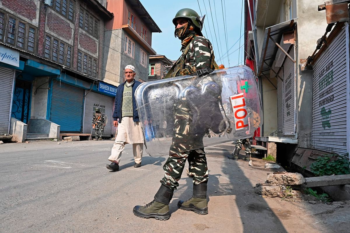 A resident walks past Indian paramilitary troopers standing guard during a lockdown in Srinagar on 29 October 2019. Photo: AFP