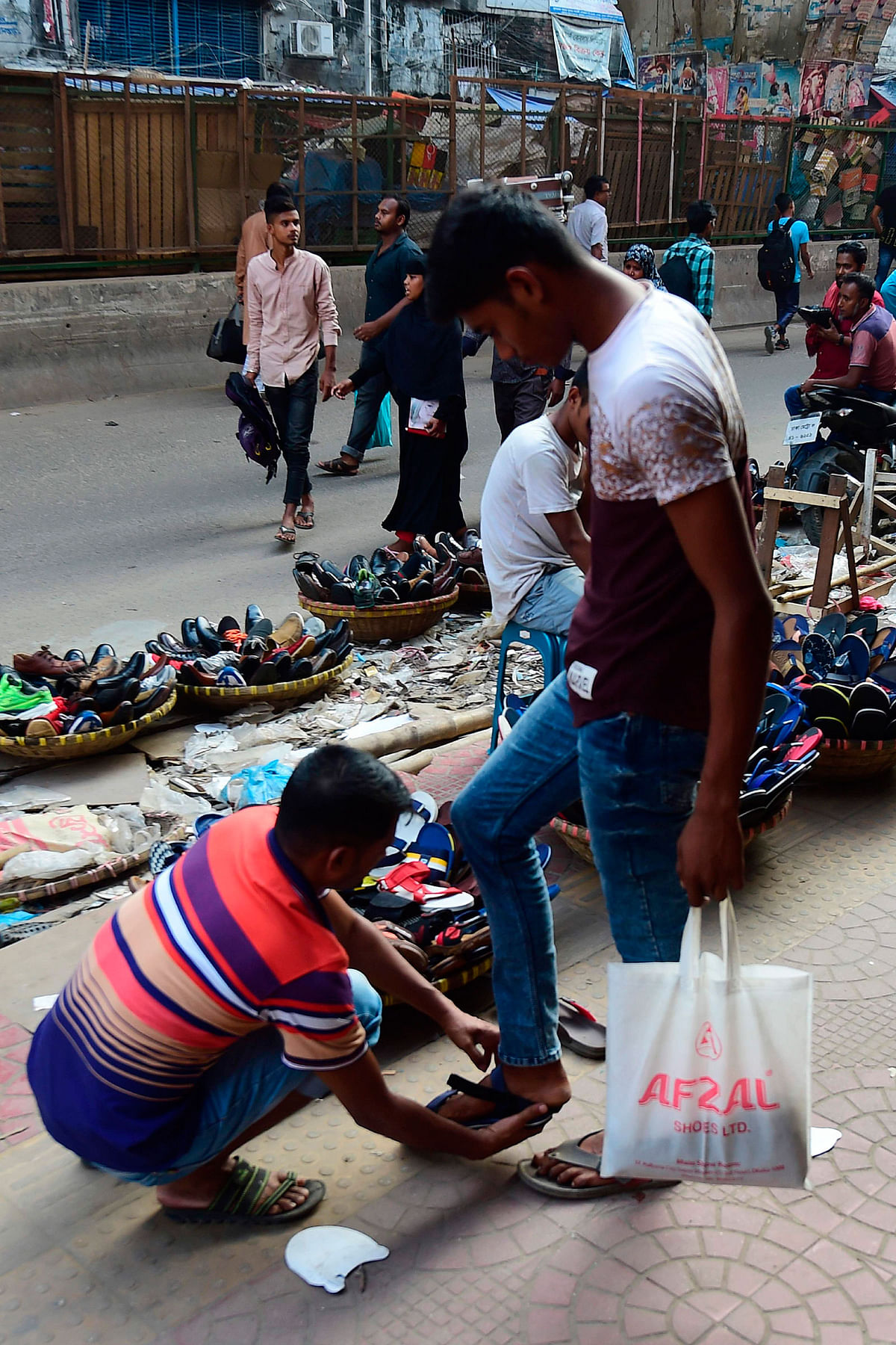 A Bangladeshi shopper tries on a shoe at a streetside shoe shop in Dhaka on 30 October 2019. Photo: AFP