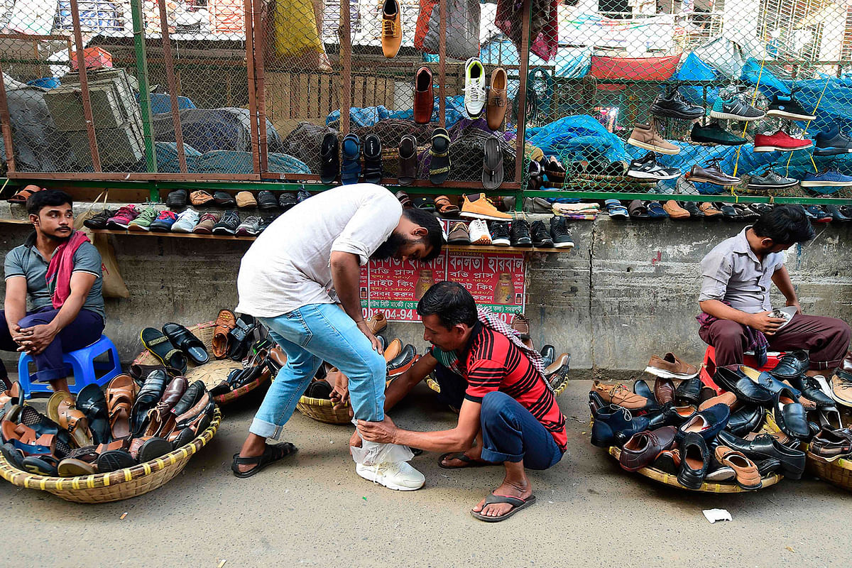 A Bangladeshi shopper tries on a shoe at a streetside shoe stall in Dhaka on 30 October 2019. Photo: AFP
