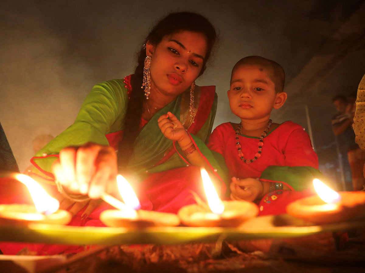 A Hindu woman lights oil lamps while sitting on the floor of a temple with her child, to observe Rakher Upabash, in Narayangonj near Dhaka, Bangladesh on 5 November 2019. Photo: Reuters