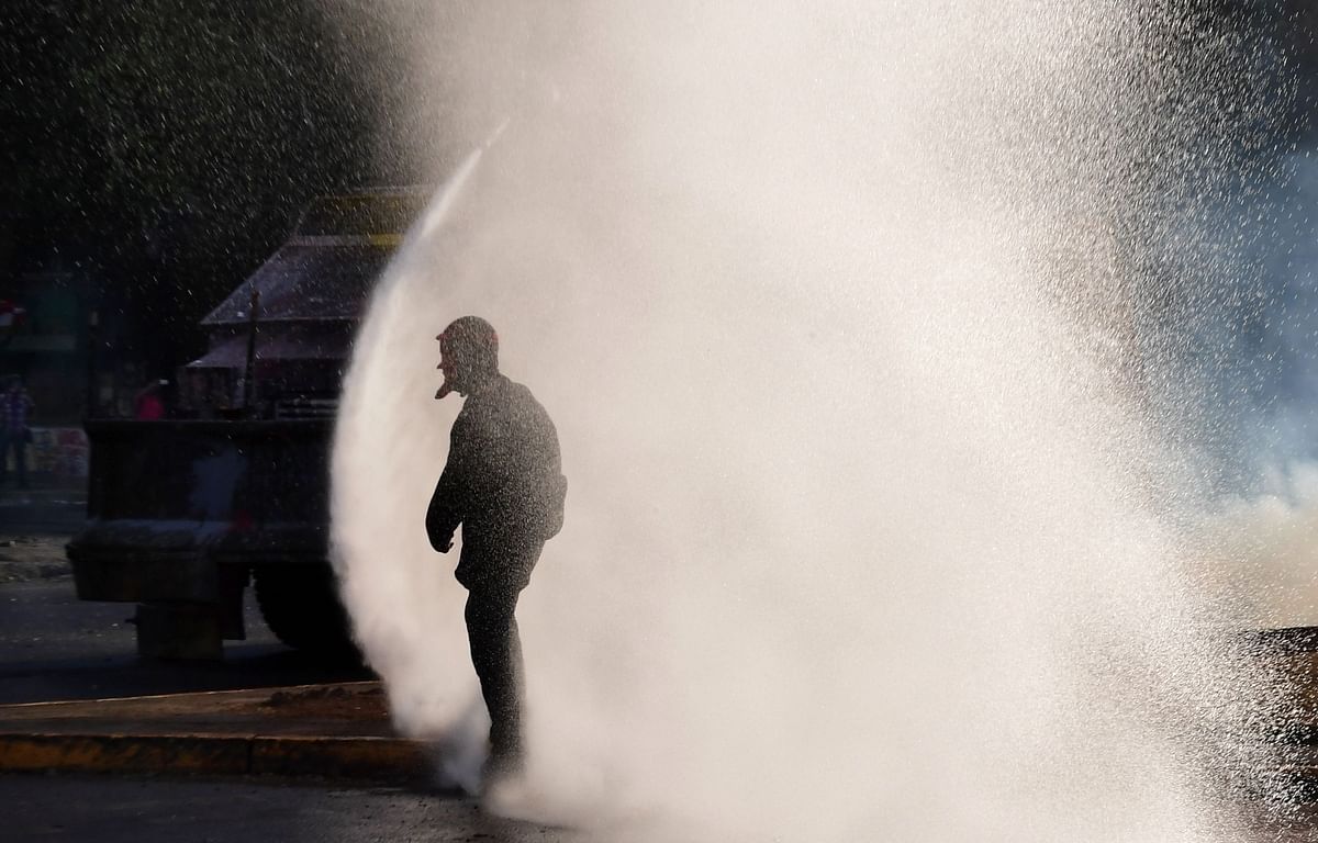 A demonstrator is sprayed with a water cannon during clashes with riot police in the surroundings of La Moneda presidential palace in Santiago on 5 November 2019. Photo: AFP