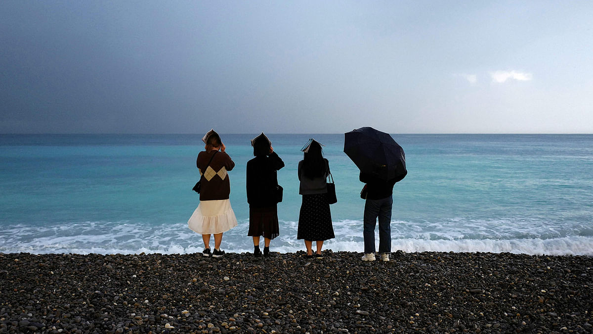 People cover their heads with an umbrella and books as they look out towards the Mediterranean Sea from the seafront during rain in the French Riviera city of Nice on 7 November 2019. Photo: AFP