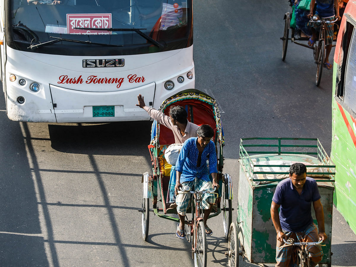 A rickshaw rider waves to a bus as the three wheeler runs on the highway violating rules on Dhaka-Narayanganj highway on 11 November 2019. Photo: Dipu Malakar