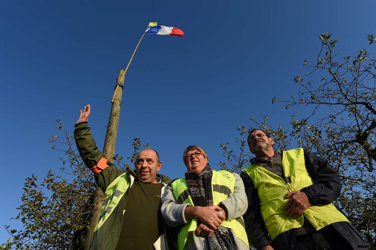 Patrick Martineau, 53, his wife Sylvie Martineau, 54, Jean-Jacques Brossay, 63, wave at cars driving on a roundabout after a weekly meeting of the `yellow vests` (Gilets Jaunes) in an orchard along the A28 motorway in Montabon, northwestern France, on 7 November. Photo: AFP