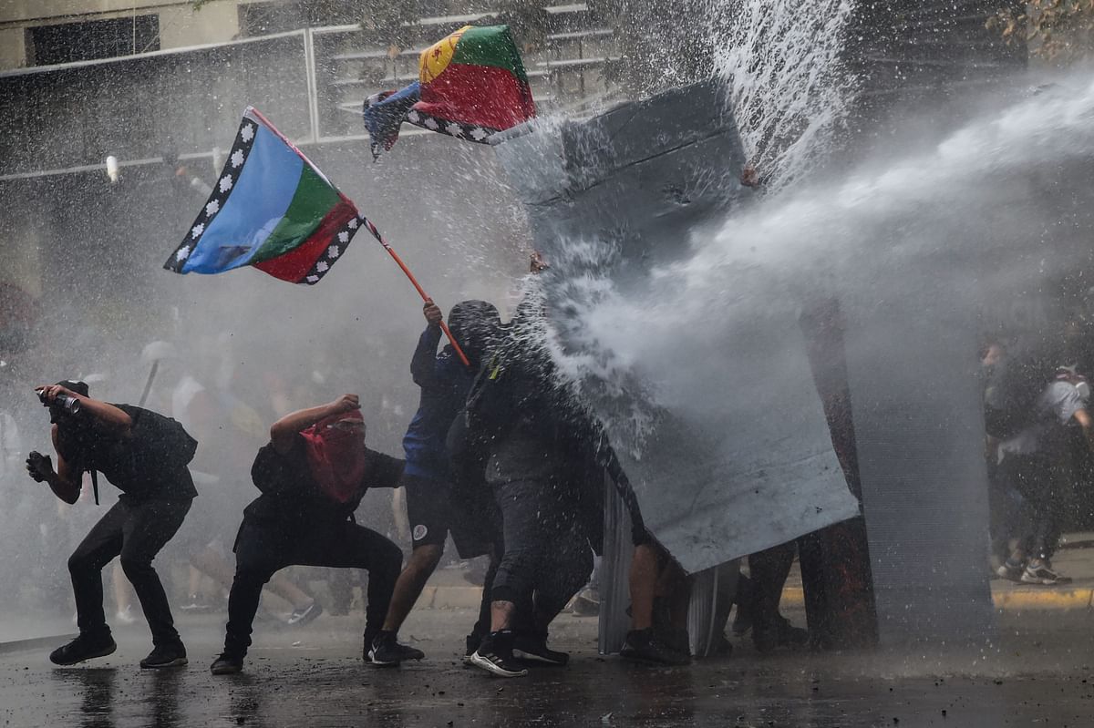 In this file picture taken on 4 November 2019 demonstrators protesting against the economic policies of the government of president Sebastian Pinera are sprayed with a water cannon during clashes with riot police in Santiago. Different countries in Latin America are currently being rocked by political change and upheaval. Photo: AFP