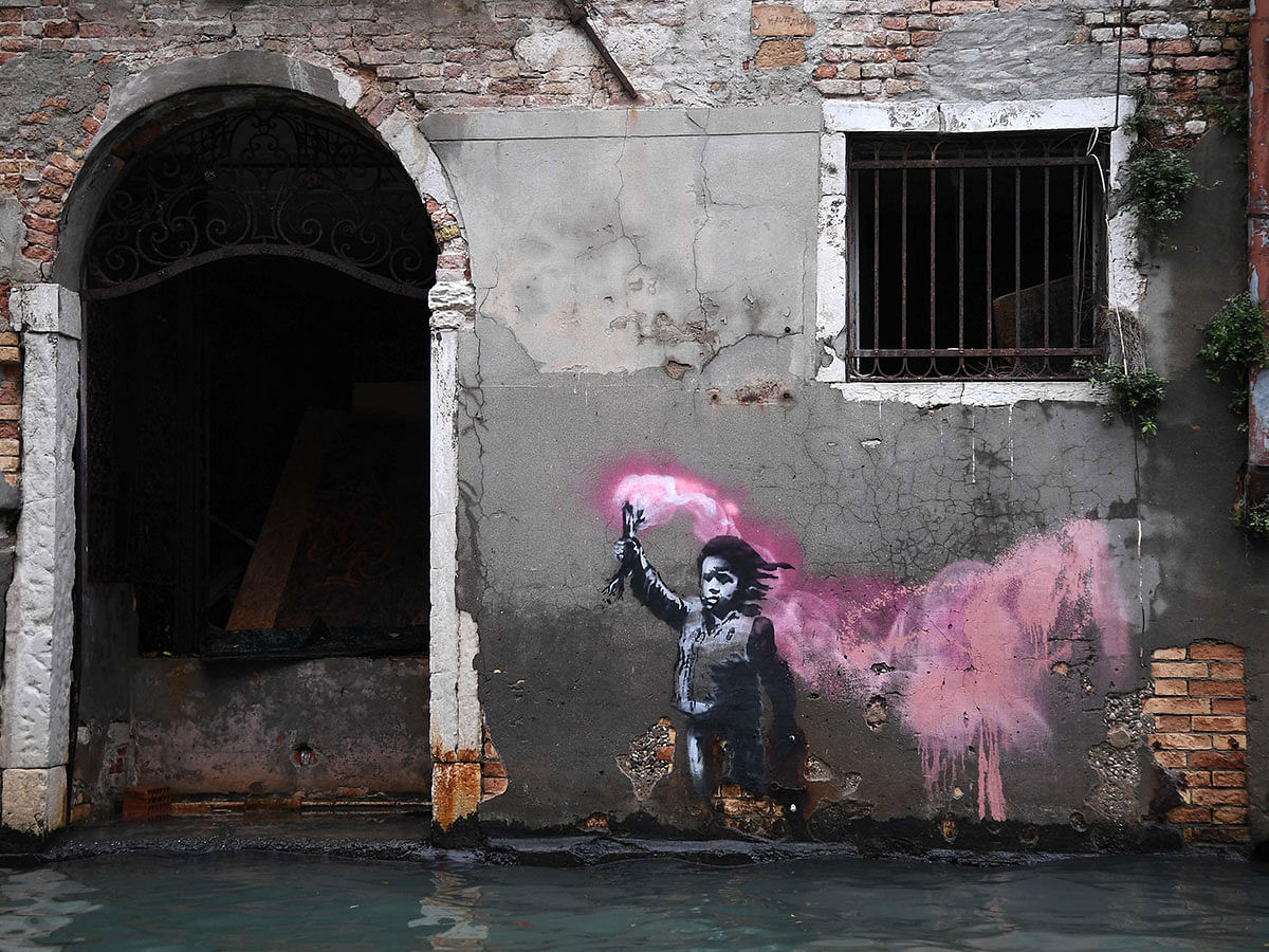 The artwork by street artist Banksy, that portrays a migrant child wearing a lifejacket and holding a neon pink flare, is pictured after an exceptional overnight `Alta Acqua` high tide water level, on 13 November in Venice. Photo: AFP
