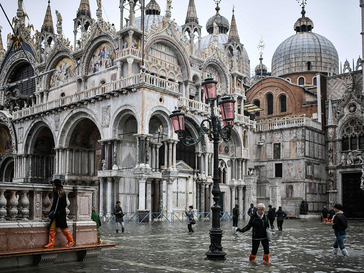 Pedestrians walk across the flooded St. Mark`s Square past St. Mark`s Basilica after an exceptional overnight `Alta Acqua` high tide water level, early on 13 November in Venice. Photo: AFP