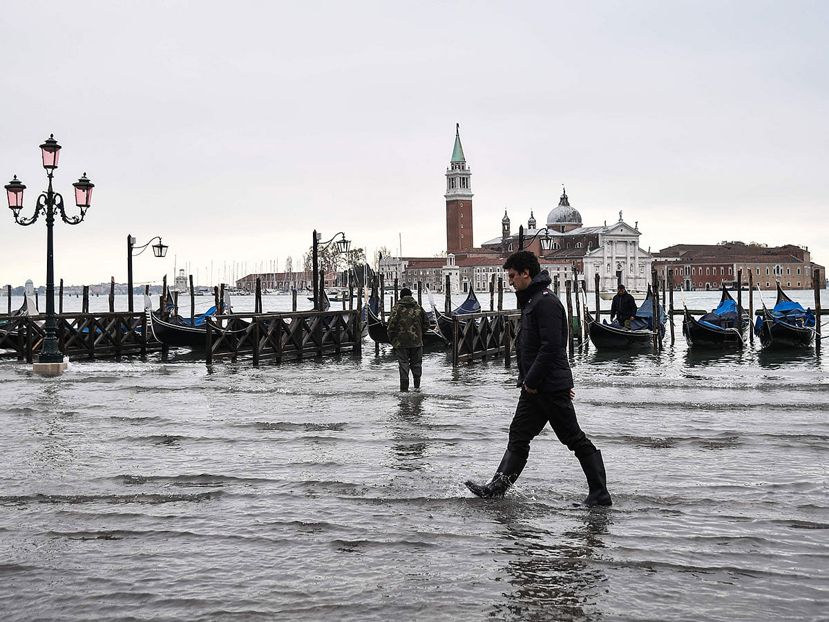A man walks across the flooded Riva degli Schiavoni embankment with the San Giorgio Maggiore basilica in background, after an exceptional overnight `Alta Acqua` high tide water level, early on 13 November in Venice. Photo: AFP