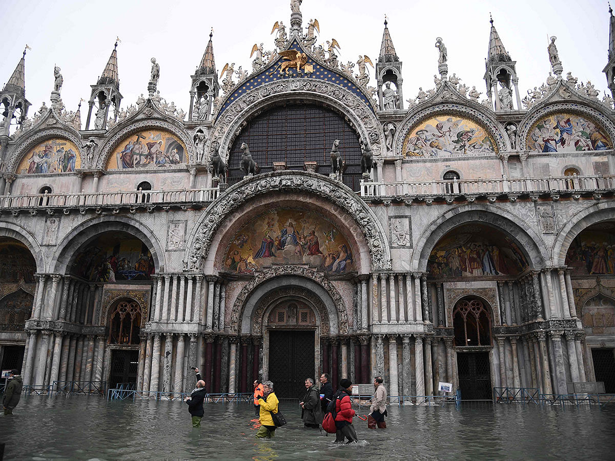 People walk across the flooded St. Mark`s square past St. Mark`s Basilica after an exceptional overnight `Alta Acqua` high tide water level, early on 13 November. Photo: AFP