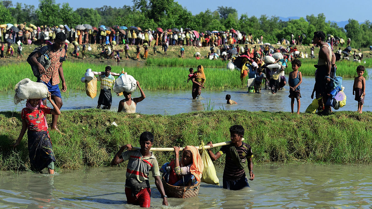 In this file photo taken on 16 October 2017 Rohingya refugees carry a woman over a shallow canal after crossing the Naf River as they flee violence in Myanmar to reach Bangladesh in Palongkhali near Ukhia. Photo: AFP