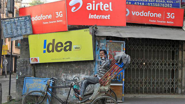 A rickshaw puller speaks on his mobile phone as he waits for customers in front of advertisement billboards belonging to telecom companies in Kolkata. Reuters file photo