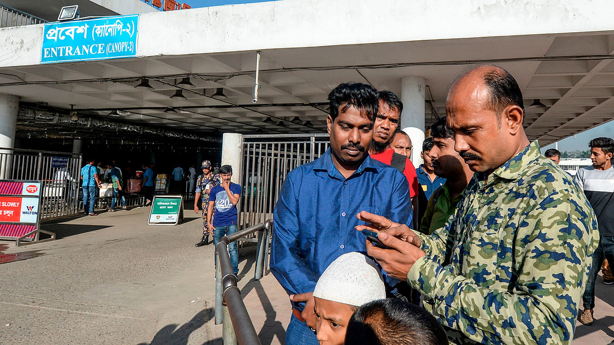 Nurul (Siraj) Islam (R) checks on a mobile phone as he waits to receive his wife Sumi Akter at Hazrat Shahjalal International Airport in Dhaka on 15 November 2019. Photo: AFP