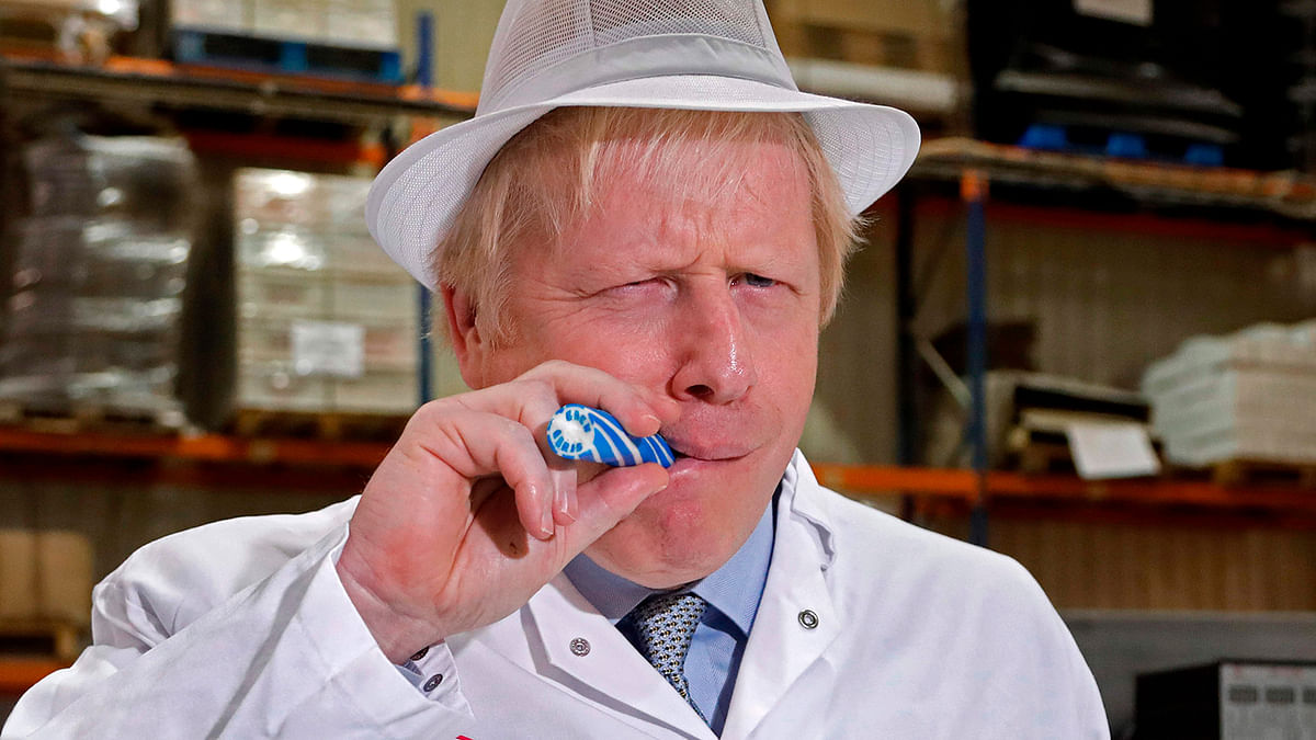 Britain`s prime minister Boris Johnson eats a stick of rock with `Back Boris` written through it during a visit to Blackpool rock producer `Coronation Candy` during a General Election campaign trail stop in north-west England on 15 November 2019. Photo: AFP
