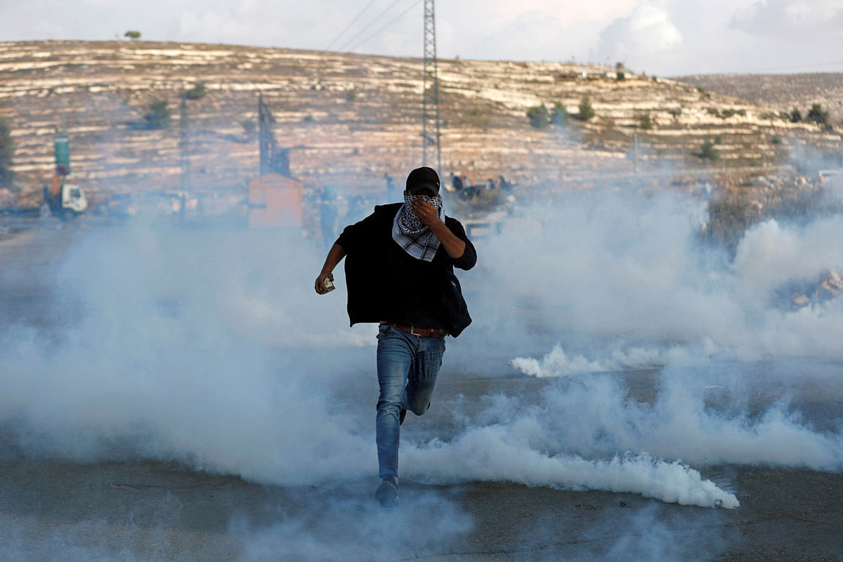 A Palestinian demonstrator runs away from tear gas fired by Israeli forces during an anti-Israel protest near the Jewish settlement of Beit El in the Israeli-occupied West Bank on 16 November. Photo: AFP