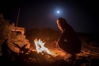 A camel herder warms up next to a fire in the desert near Dakhla in Morocco-administered Western Sahara on 13 October 2019. Photo: AFP