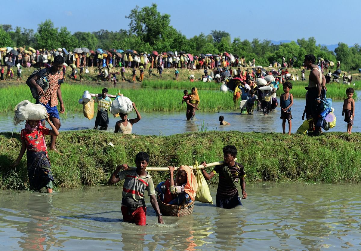 In this file photo taken on 16 October 2017 Rohingya refugees carry a woman over a shallow canal after crossing the Naf River as they flee violence in Myanmar to reach Bangladesh in Palongkhali near Ukhia. Photo: AFP