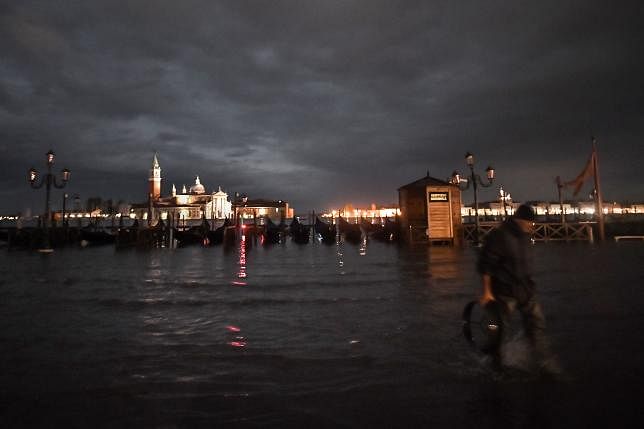 A man walks across the flooded embankment by the Venetian lagoon on the side of St. Peter`s Square during an exceptional `Alta Acqua` high tide water level late on 12 November in Venice. Photo: AFP