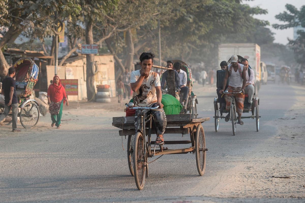 A man riding a three-wheeler cart (C) gestures as he rides on a road under heavy smog conditions in Dhaka on 26 November 2019. Photo: AFP