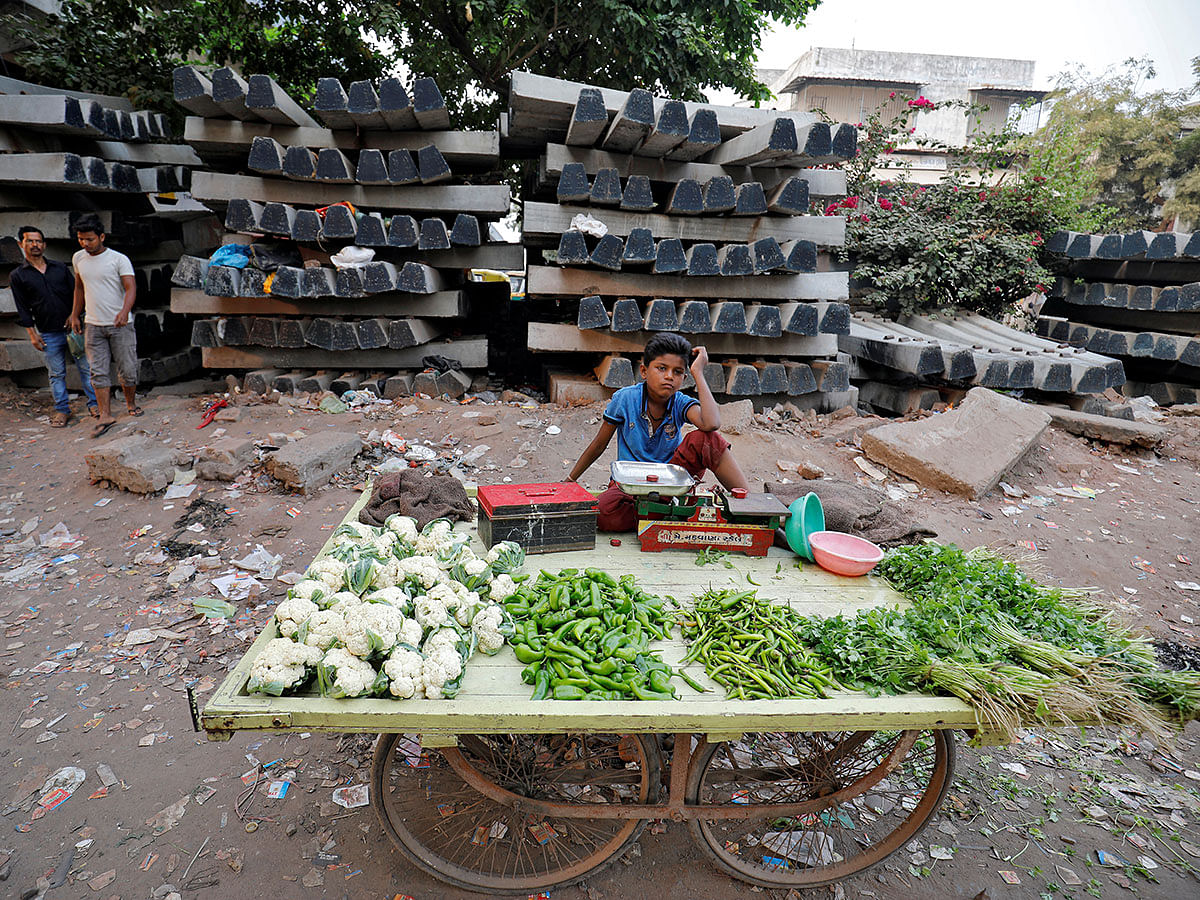 A boy selling vegetables waits for customers in front of construction material for railway tracks, at Navapura on the outskirts of Ahmedabad, India, on 28 November 2019. Photo: Reuters