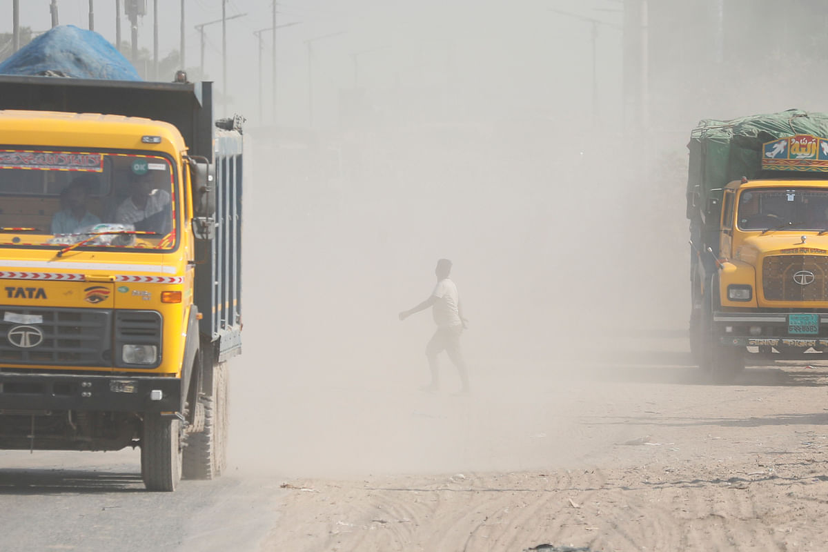A man crosses a road while trucks ply along the road amid huge dust at Amin Bazar, Dhaka on 27 November. Photo: Ashraful Alam
