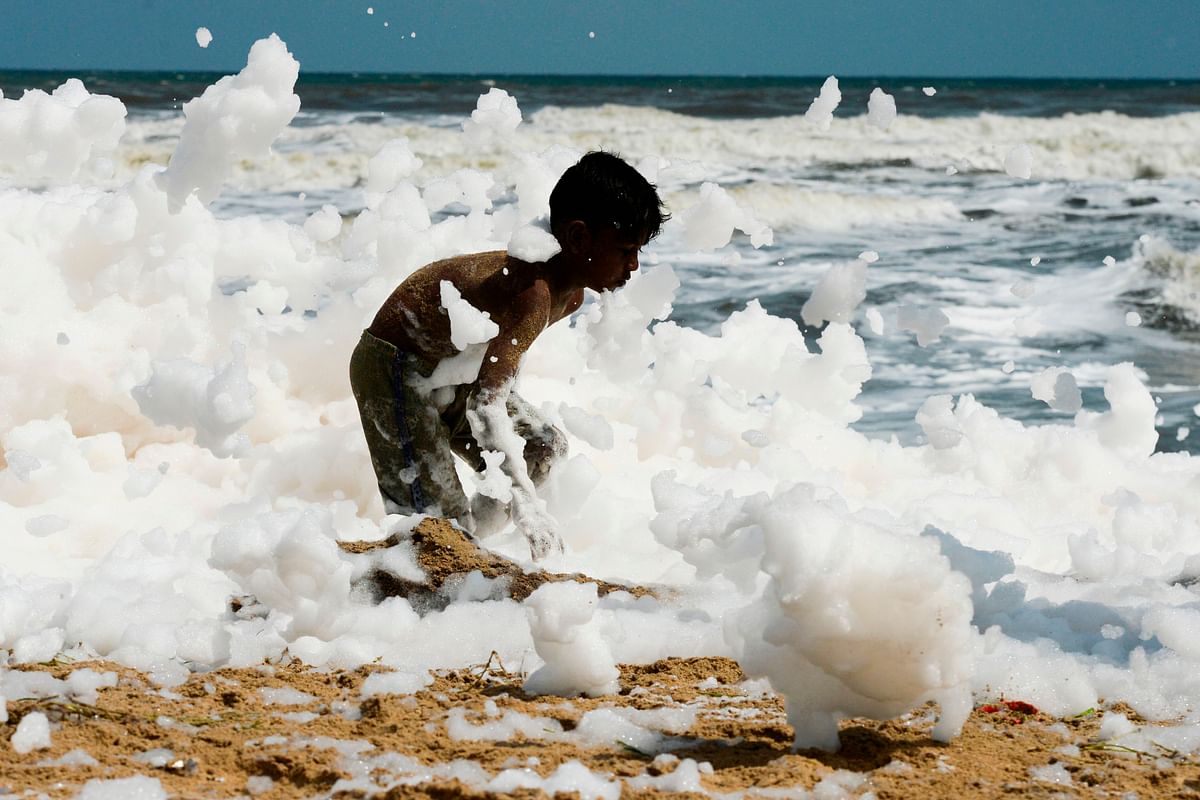 A youth plays over foamy discharge, caused by pollutants, as it mixes with the surf at a beach in Chennai on 29 November 2019. Photo: AFP