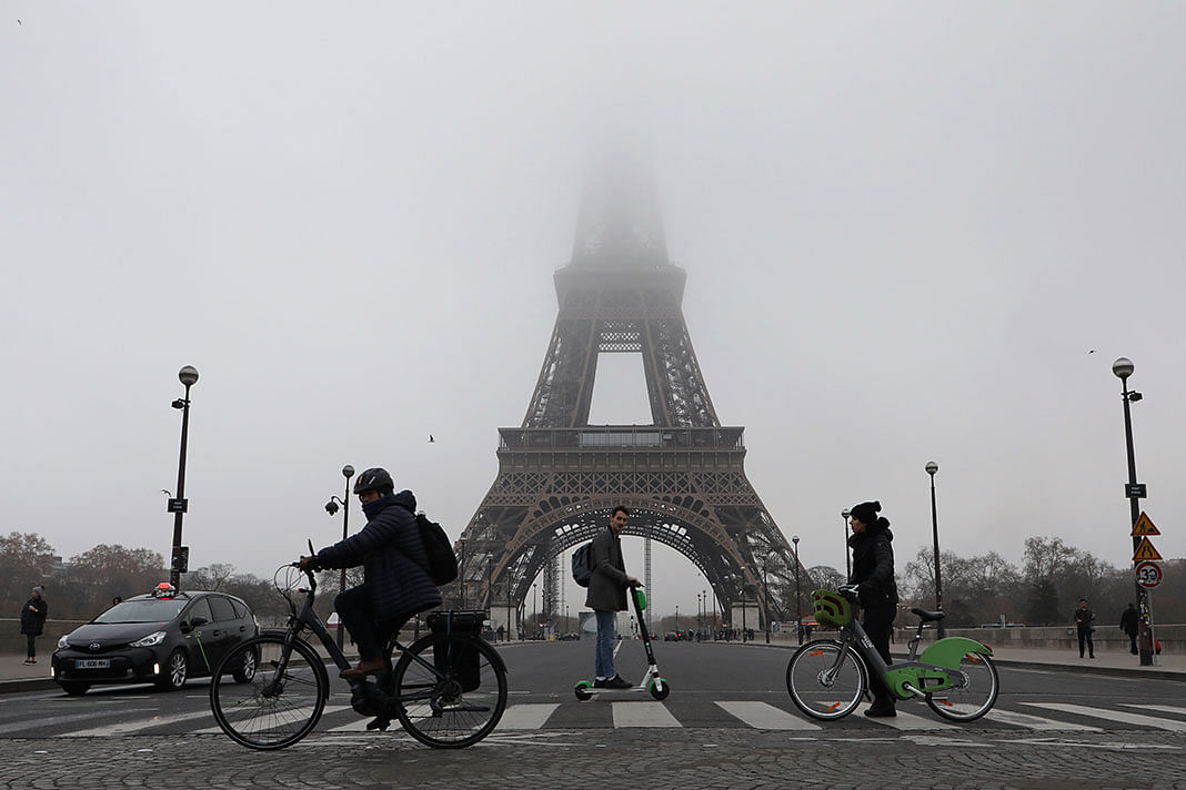People ride bicycles and electric scooter past the Eiffel tower partially hidden by fog, on Thursday in Paris, as the monument is closed to the public due to a nationwide strike against the government`s plans for a `universal` pension system they say will force millions of people to work longer. Photo: AFP