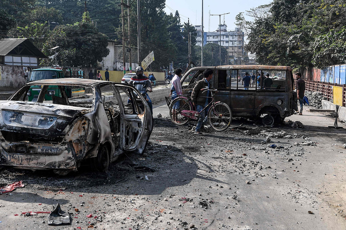 People make their way among the remains of gutted vehicles on a road in Guwahati on 13 December, 2019, a day after protests against the government`s Citizenship Amendment Bill (CAB) broke out across India`s northeastern state of Assam. Photo: AFP