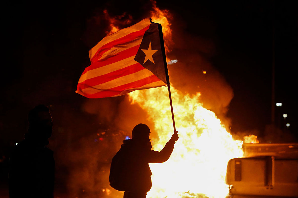 A protester waving a Catalan pro-independence `Estelada` flag stands next to a burning barricade during a protest called by Catalan separatist movement Democratic Tsunami outside the Camp Nou stadium in Barcelona on 18 December 2019, during the `El Clasico` Spanish League football match between Barcelona FC and Real Madrid CF. Photo: AFP