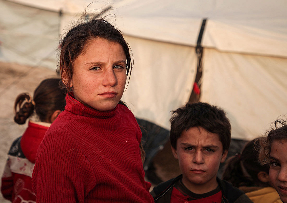 Syrian children, among those who fled from government forces` advance on Maaret al-Numan in the south of Idlib prvoince, look on as they stand outside tents at a camp for the displaced near the town of Dana in the province`s north near the border with Turkey, on 27 December 2019. Photo: AFP