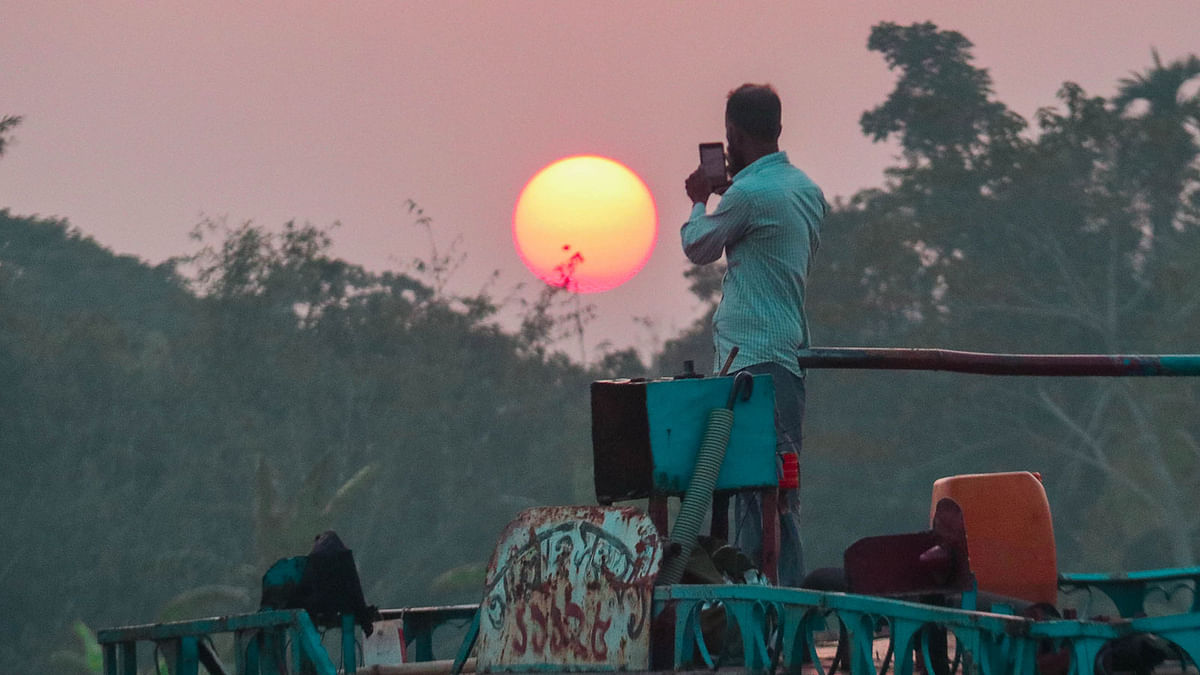 A trawler driver takes photographs of sunset from Bhairab river in Khulna on 28 December, 2019. Photo: Saddam Hossain