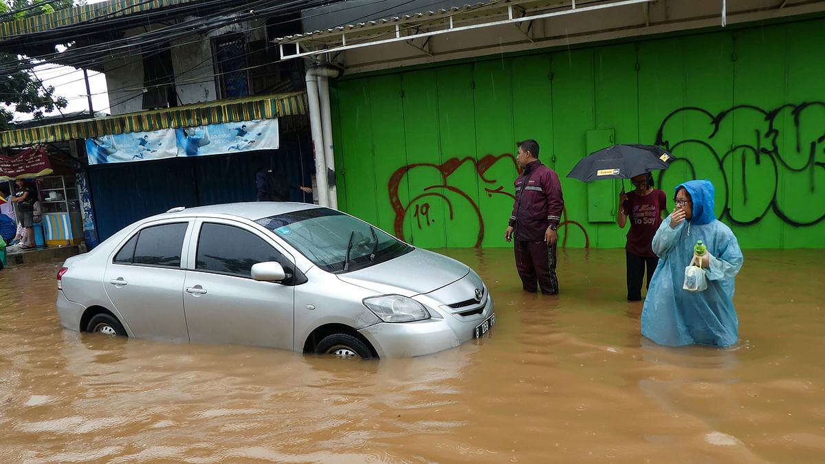 People walk past a car stuck in floodwaters after rain all night caused local flooding in Jakarta on 1 January 2020. Photo: AFP