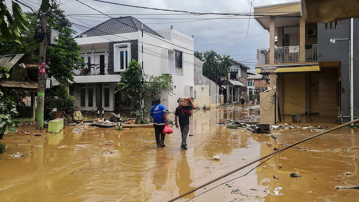 Indonesians carrying supplies walk through a muddy street at a housing complex in Bekasi, West Java on 2 January 2020, after flooding triggered by heavy rain hit the area. Photo: AFP