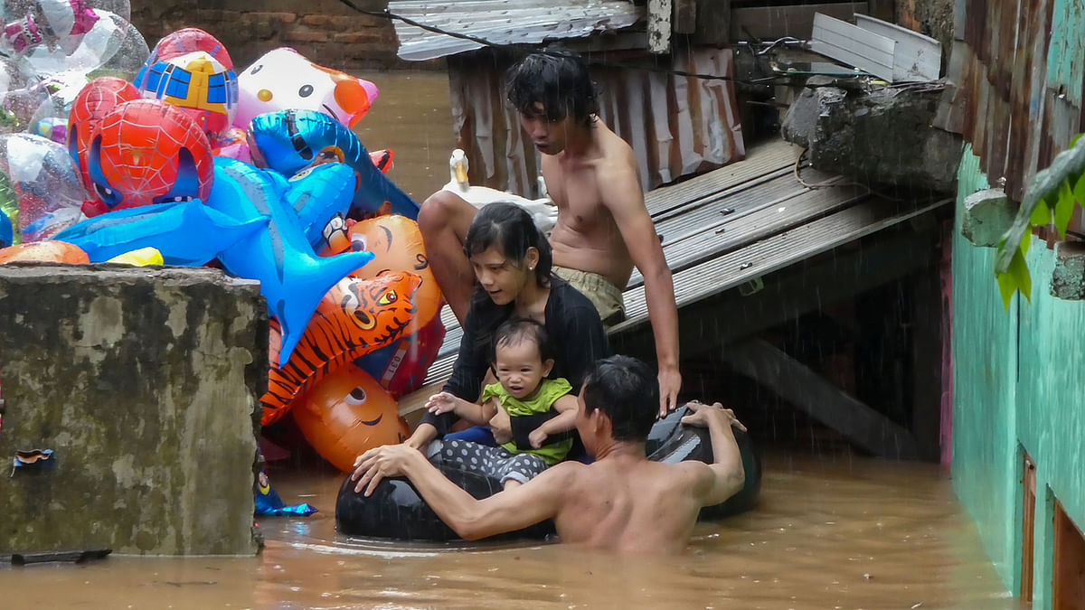 A family evaculate their home by using an inflated inner-tube after rain all night caused local flooding in Jakarta on 1 January 2020. Photo: AFP