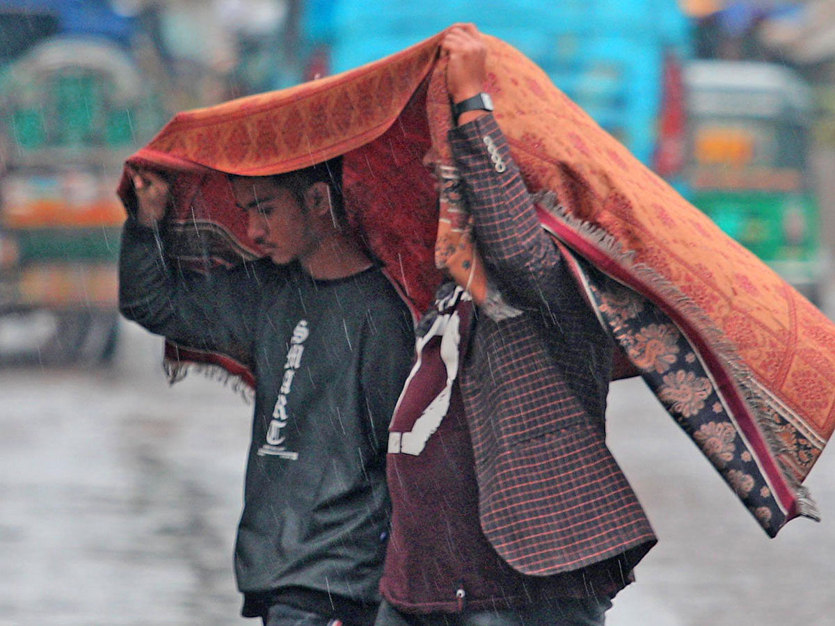 Two men cover them under a cloth in the rain while crossing a road at GEC intersection in Chattogram on 3 January 2019. Photo: Jewel Shill