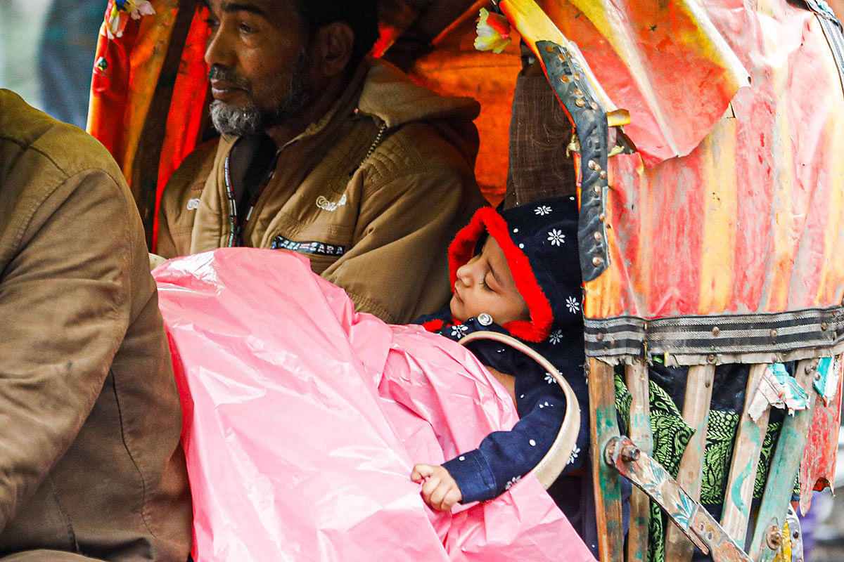 Man with a child asleep in a rickshaw during a drizzle at Science Laboratory intersection, Dhaka on 3 January 2019. Photo: Dipu Malakar