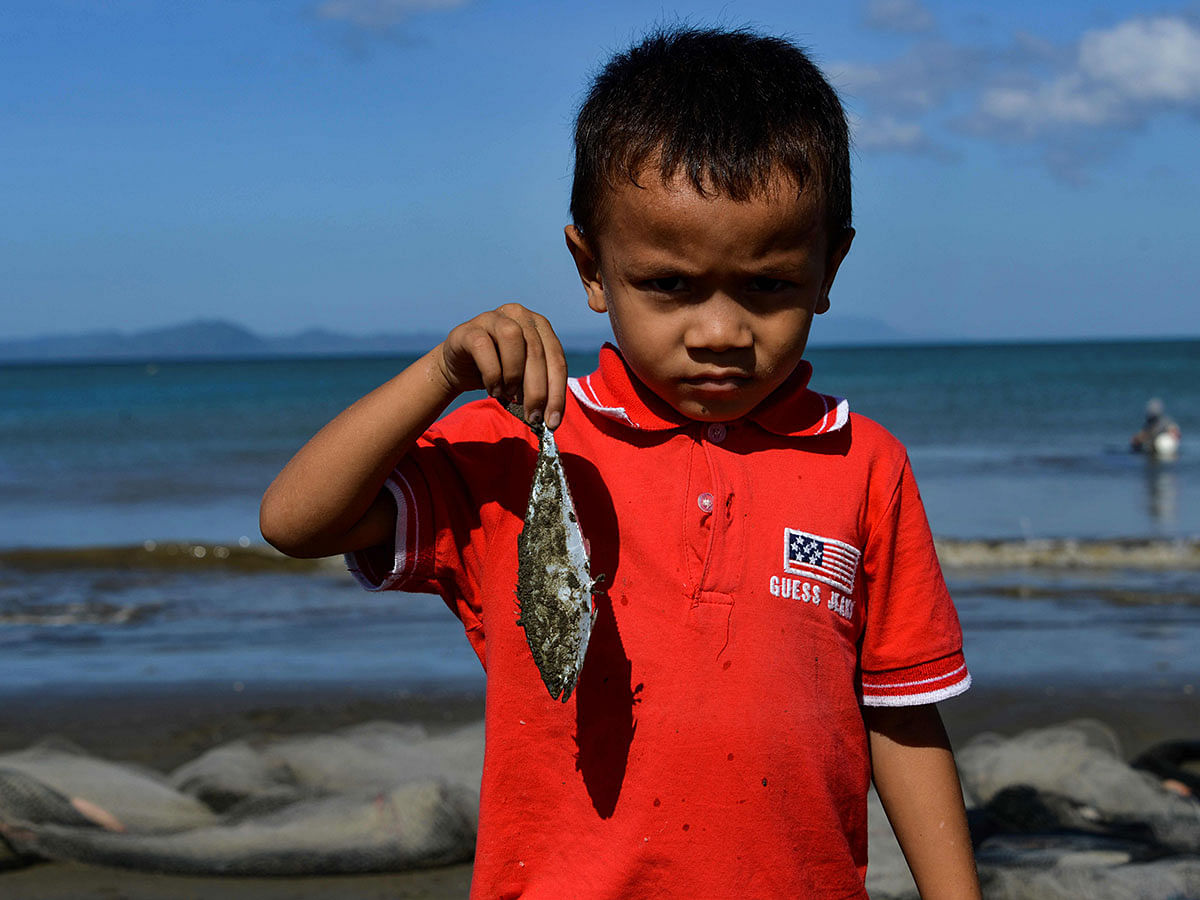 A child shows a fish caught in a fishing net on a beach in Banda Aceh on 2 January 2020. Photo: AFP