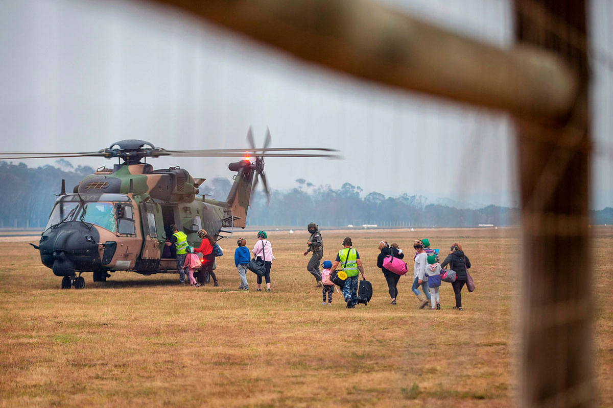 This handout photo taken on 5 January 2020 and received on 6 January from the Australian Department of Defence shows Civilian evacuees boarding a Royal Australian Navy MRH-90 helicopter at Mallacoota, as bushfires threaten the area. Photo: AFP
