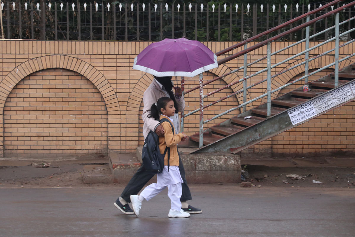 A man and a girl walk along a road with an umbrella in a drizzle during a cold day at Surma Point, Sylhet on 5 January 2019. Photo: Anis Mahmud