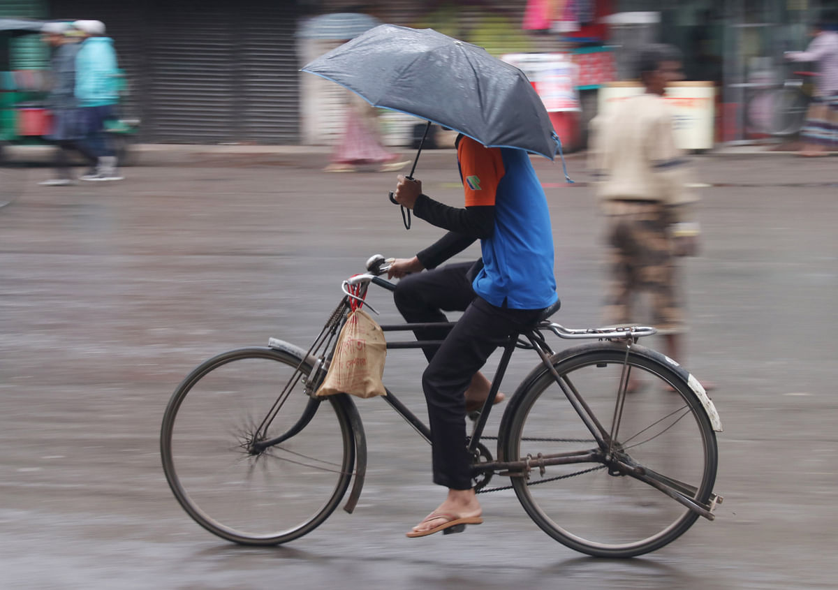 A man rides a bicycle with an umbrella in a drizzle during a cold day at Surma Point, Sylhet on 5 January. Photo: Anis Mahmud