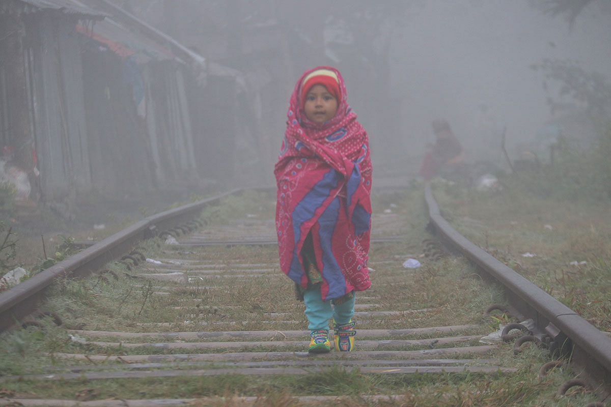 A child, covered in warm clothes, walks along a railway line in a cold morning at Daulatpur, Khulna on 7 January 2019. Photo: Saddam Hossain