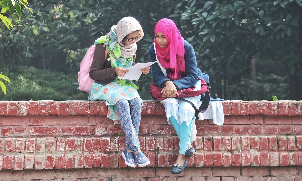 Two students look over a shit of paper while basking in the sun at Khulna University on 8 January 2019. Photo: Saddam Hossain