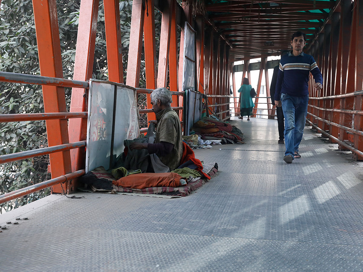 A pedestrian walks past a homeless man sitting on makeshift bed on an over-bridge at Shukrabad, Dhaka on 3 January 2019. Photo: Sabina Yesmin
