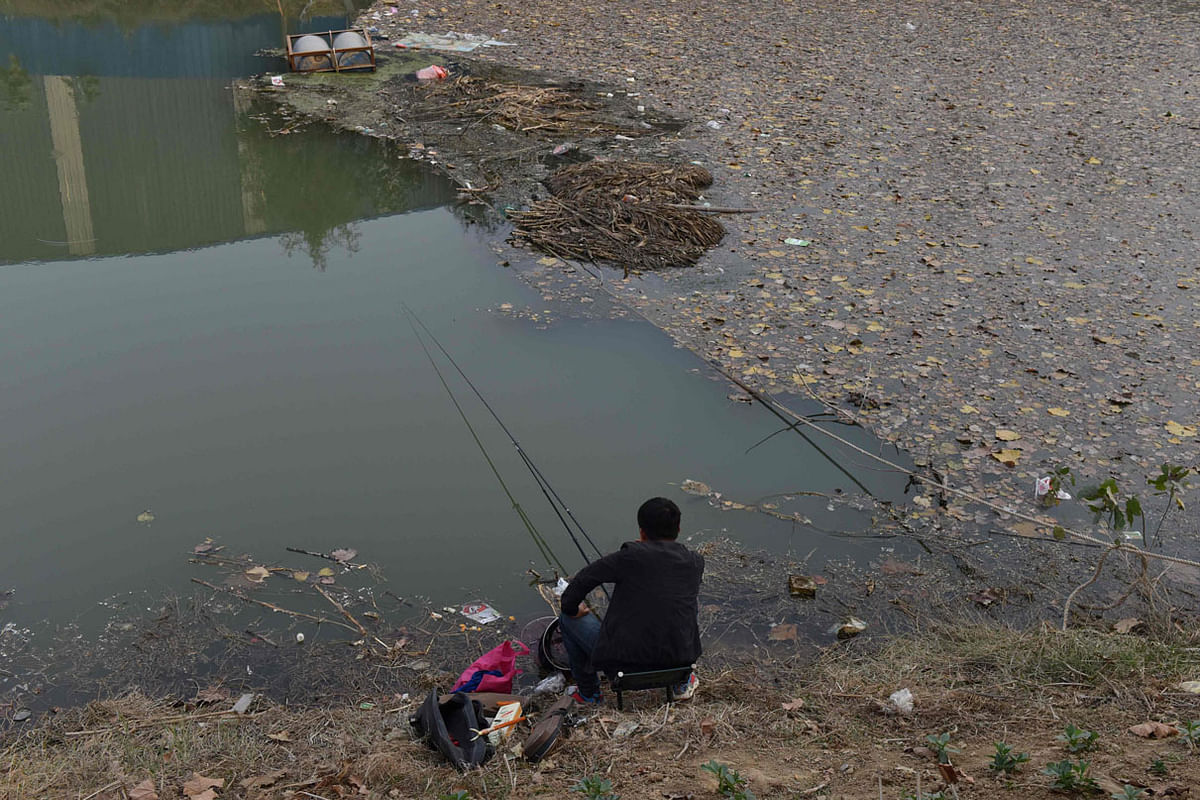 This photo taken on 8 November 2019 shows a man fishing near leaves collecting in a canal in Shenqiu, in China`s central Henan province. Photo: AFP