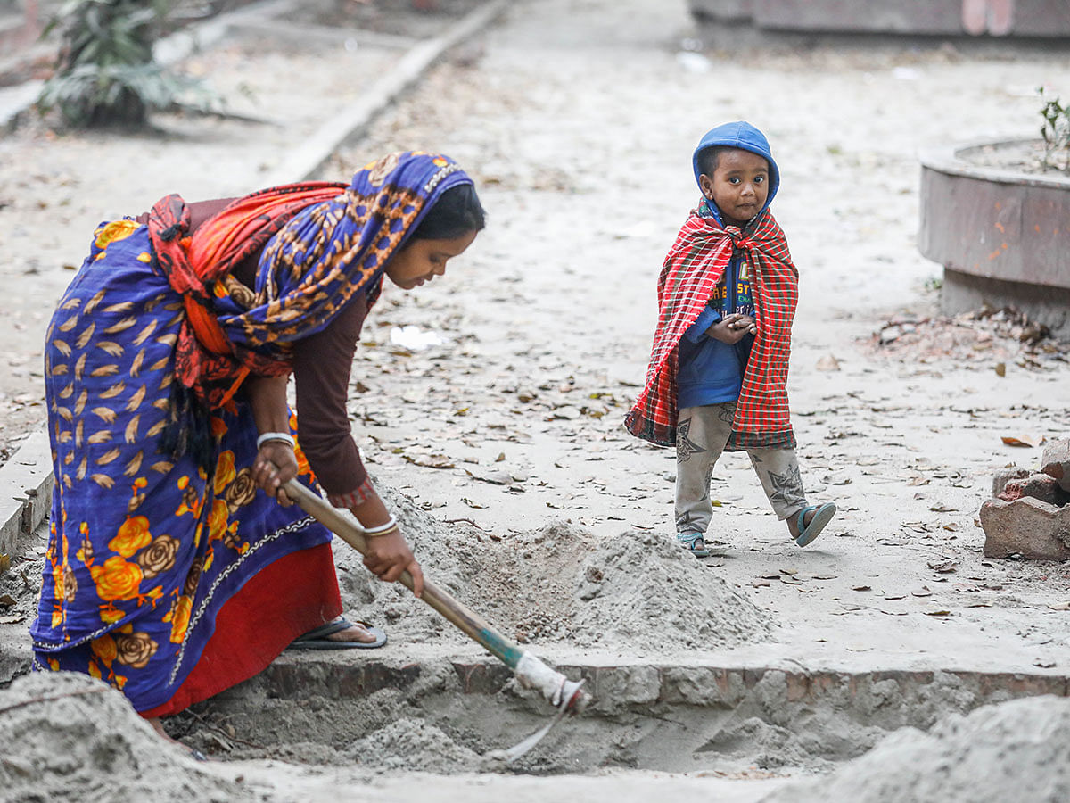 A child covered in gamchha (a local towel) walks as his mother digs sand on Hair Road near Ramna Park area of Dhaka on 11 January 2019. Photo: Dipu Malakar